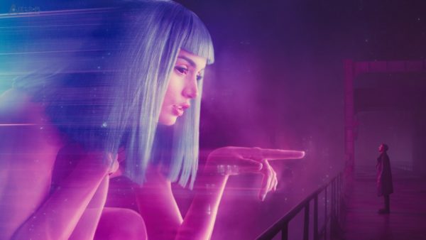 Kadr z filmu „Blade Runner 2049”, główny bohater stoi naprzeciw gigantycznej holograficznej reklamy Joi – sztucznej inteligencji mającej dotrzymywać towarzystwa samotnemu klientowi